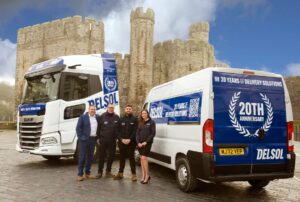 A photo of four members of the Delsol team celebrating 20 years in front one of the company's trucks and a van and a castle in the background