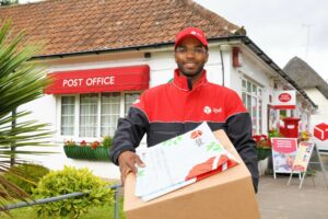 A DPD delivery person standing outside a post office while holding a parcel box and some packages