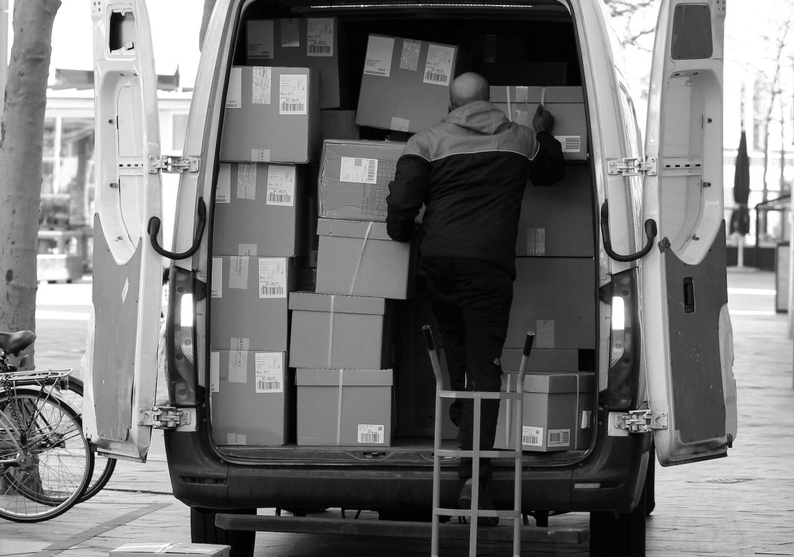 black and white photograph of a delivery driver loading boxes in the back of a large van